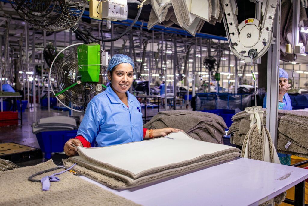 Female textile worker smiling at camera in a modern, organized factory setting.